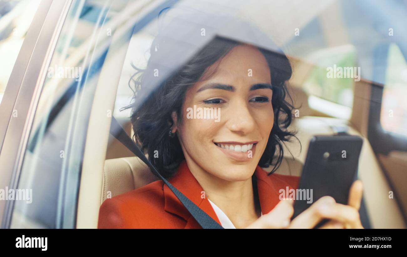 Schöne lächelnde Frau Reisen in einem Auto, sitzen auf einem Beifahrersitz verwendet Smartphone, Typen Nachricht, browses through Internet. Kamera aufgenommen von Stockfoto