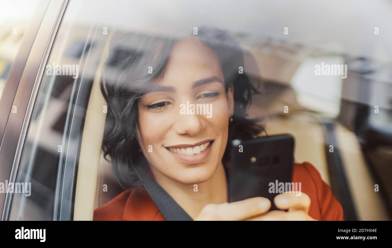 Schöne Frau Reisen in einem Auto, sitzen auf einem Beifahrersitz verwendet Smartphone, Typen Nachricht, browses through Internet. Kamera Aufnahme von außerhalb des Stockfoto