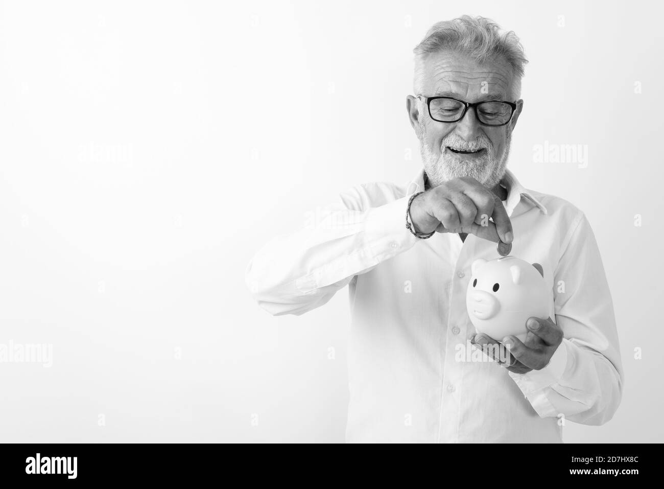 Studio shot von Happy älterer bärtiger Mann lächelnd, während sie und die Münze in Sparschwein mit Brille vor weißem Hintergrund Stockfoto