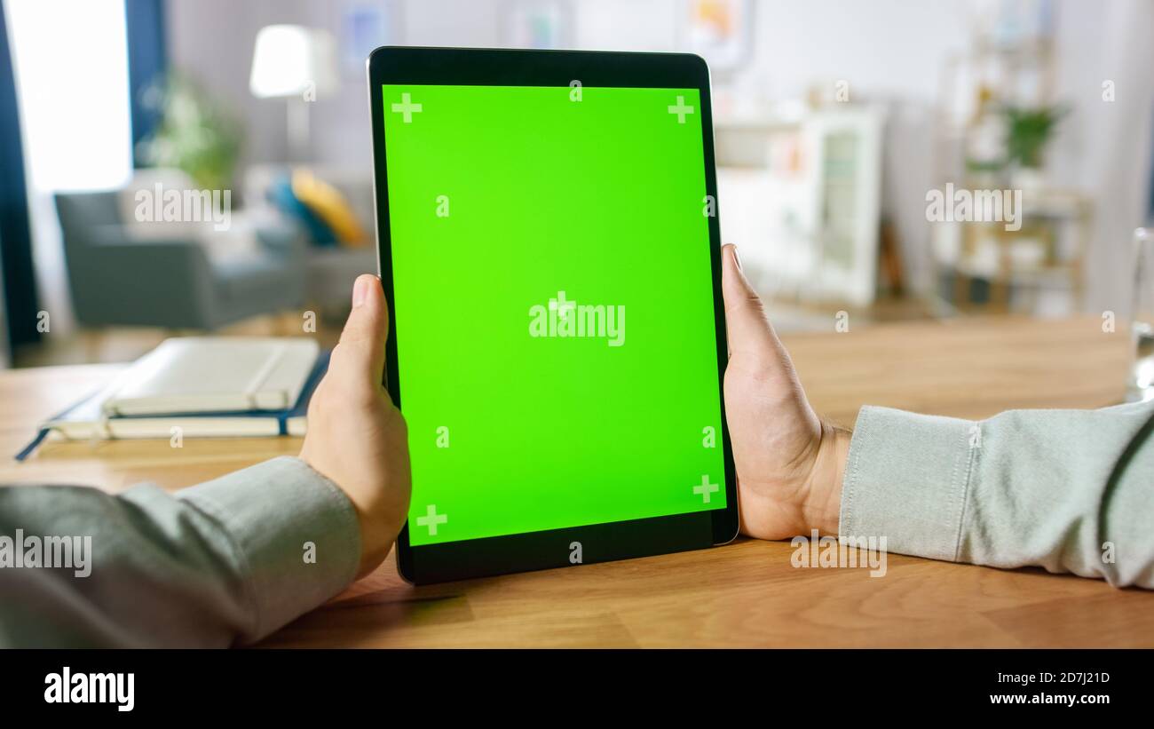 First Person Shot of man mit Handgesten auf Green Mock-Up Screen Digital Tablet Computer im Portrait-Modus, während er an seinem Schreibtisch sitzt. Im Stockfoto