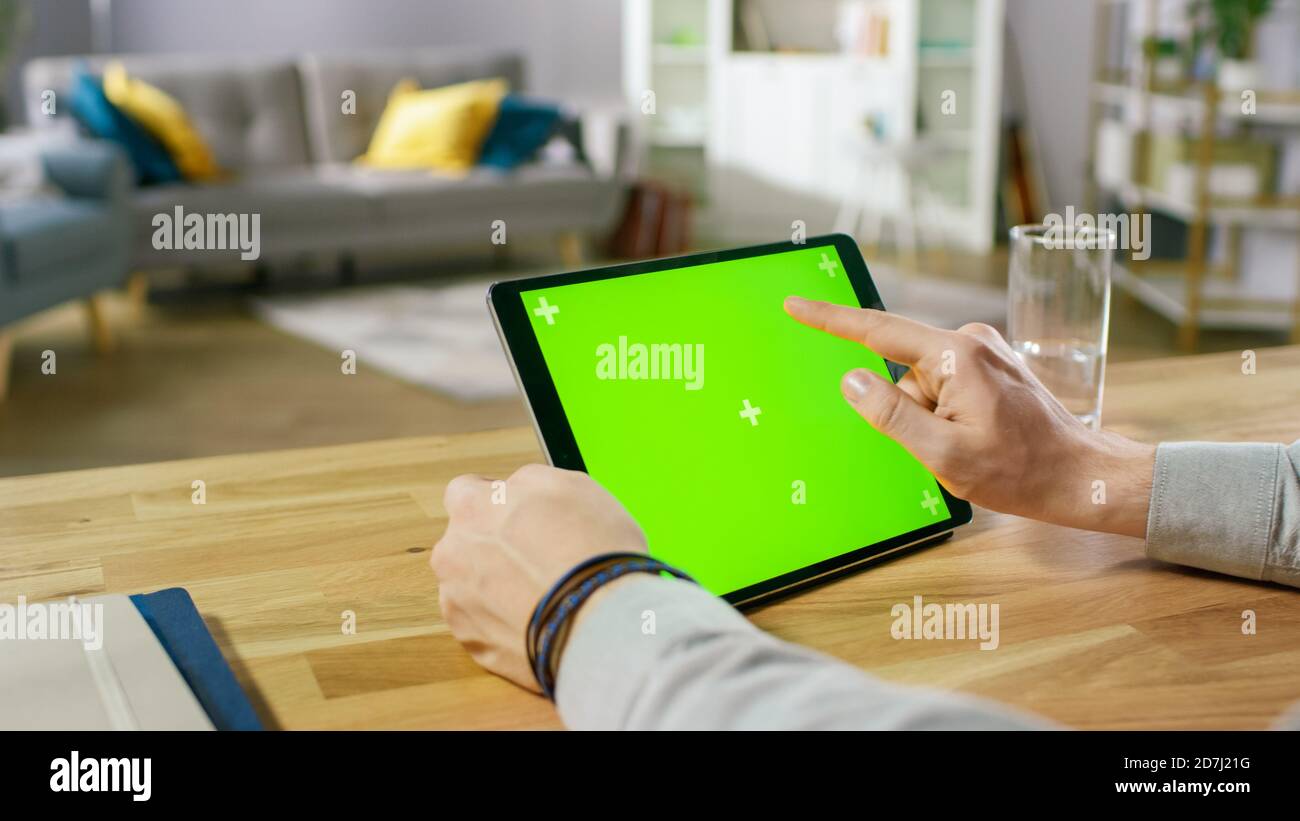 Mann hält und mit Handgesten auf Green Mock-up-Bildschirm Digital Tablet-Computer, während Sie am Schreibtisch sitzen. Mann, der Sachen kauft oder durchläuft Stockfoto