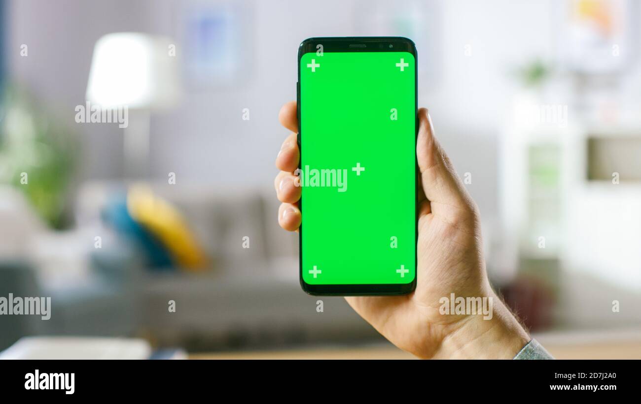 Nahaufnahme des Menschen mit Handgesten auf dem grünen Mock-up-Bildschirm Digital Tablet Computer im Portrait-Modus, während er an seinem Schreibtisch sitzt. Im Hintergrund gemütlich Stockfoto