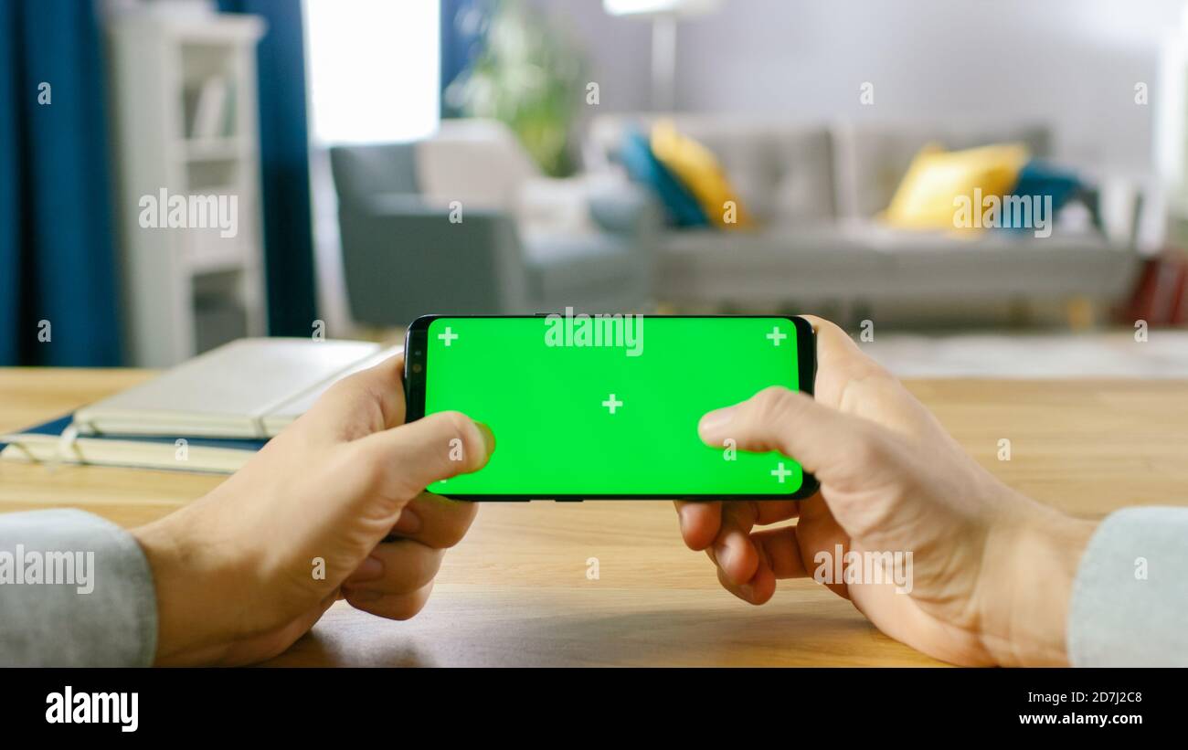 Erste Person Nahaufnahme des Mannes halten Green Screen Smartphone im Landscape-Modus und Spiel mit seinen Daumen. Stockfoto