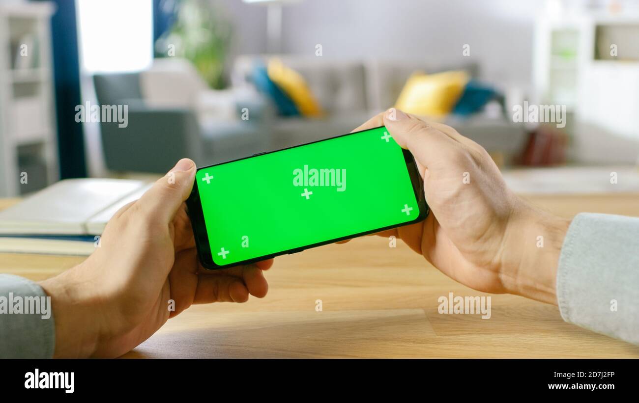 Erste Person Nahaufnahme des Mannes halten Green Screen Smartphone Im Landschafts-Modus und in einem Racing-Videospiel spielen Durch Neigen des Mobiltelefons Stockfoto