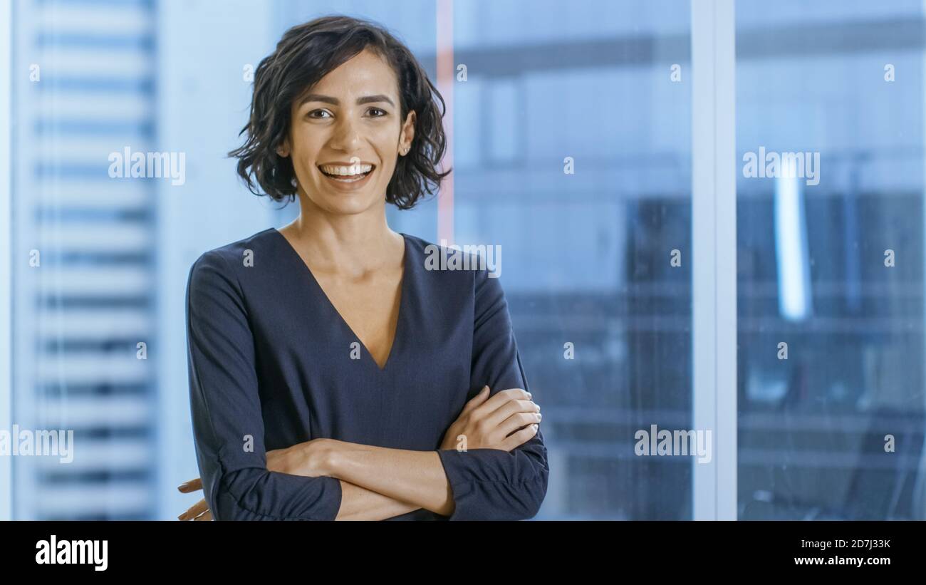 Porträt der erfolgreichen Geschäftsfrau, die ihre Arme und Smiles überquert. Schöne Frau Executive stehend in ihrem Büro. Stockfoto