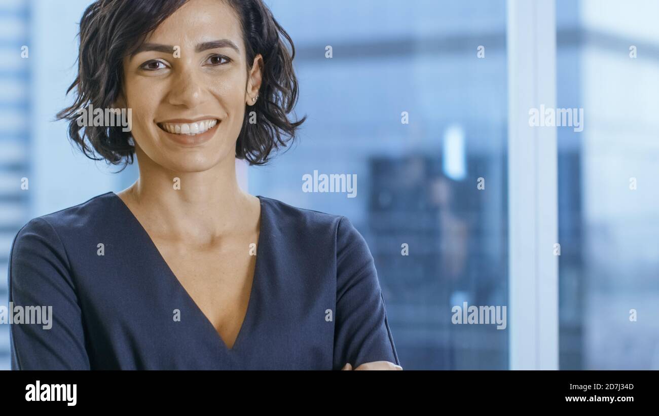 Porträt der erfolgreichen hispanischen Geschäftsfrau, die ihre Arme überquert und lächelt. Schöne weibliche Executive stehend in ihrem Büro. Stockfoto