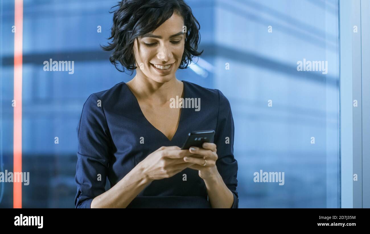 Nahaufnahme der schönen hispanischen Frau mit Smartphone. Business Lady in formelle Kleidung Kleid Eingabe von Nachrichten auf Handy. Im Hintergrund Stockfoto