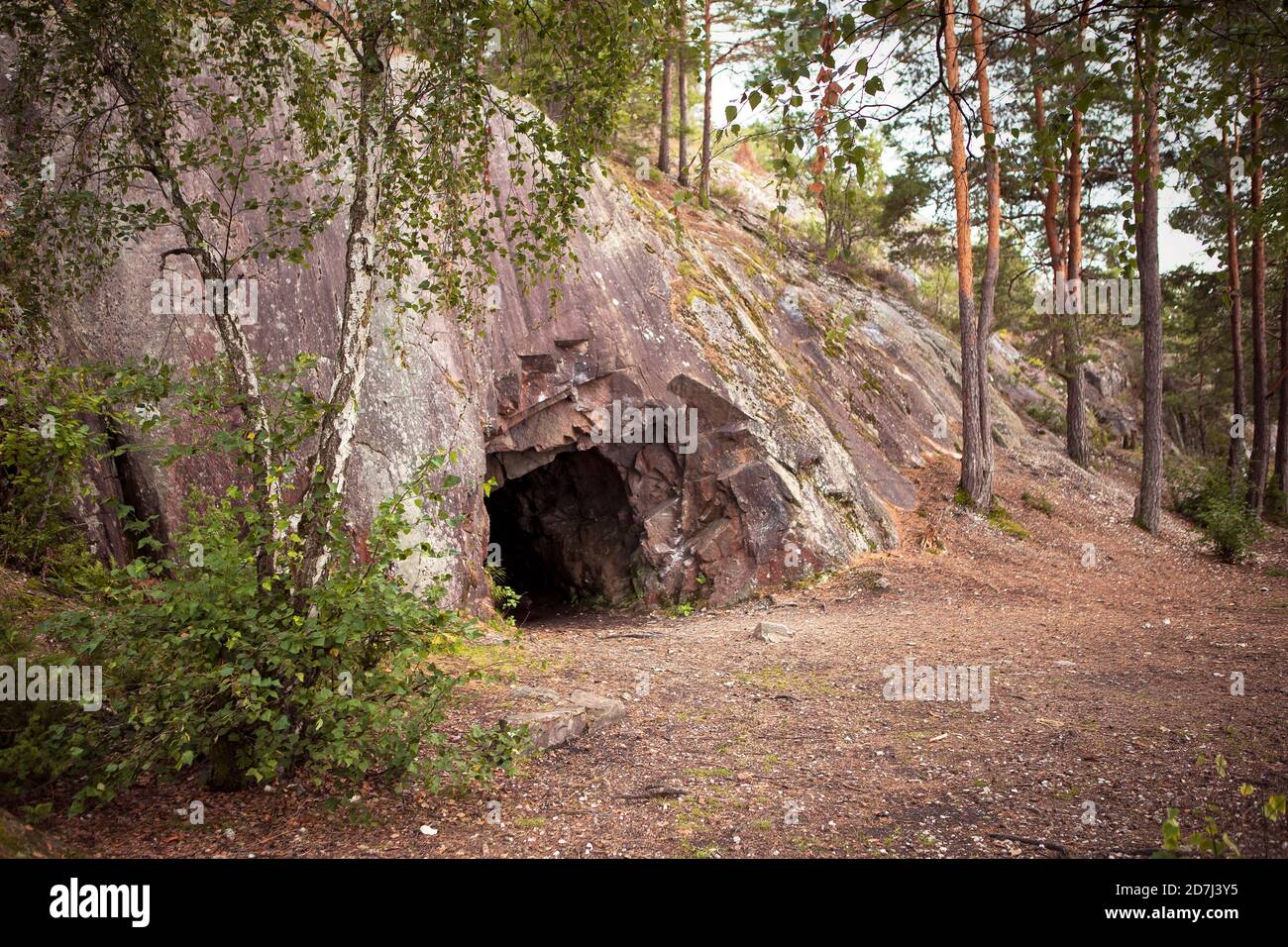 Landschaft mit Höhle und Wald. Landschaftlich schöner Eingang zur Höhle. Felswand mit einem dunklen Loch. SPRO, historische Mineralmine. Nesodden Norwegen. Nesoddtangen-Penine Stockfoto