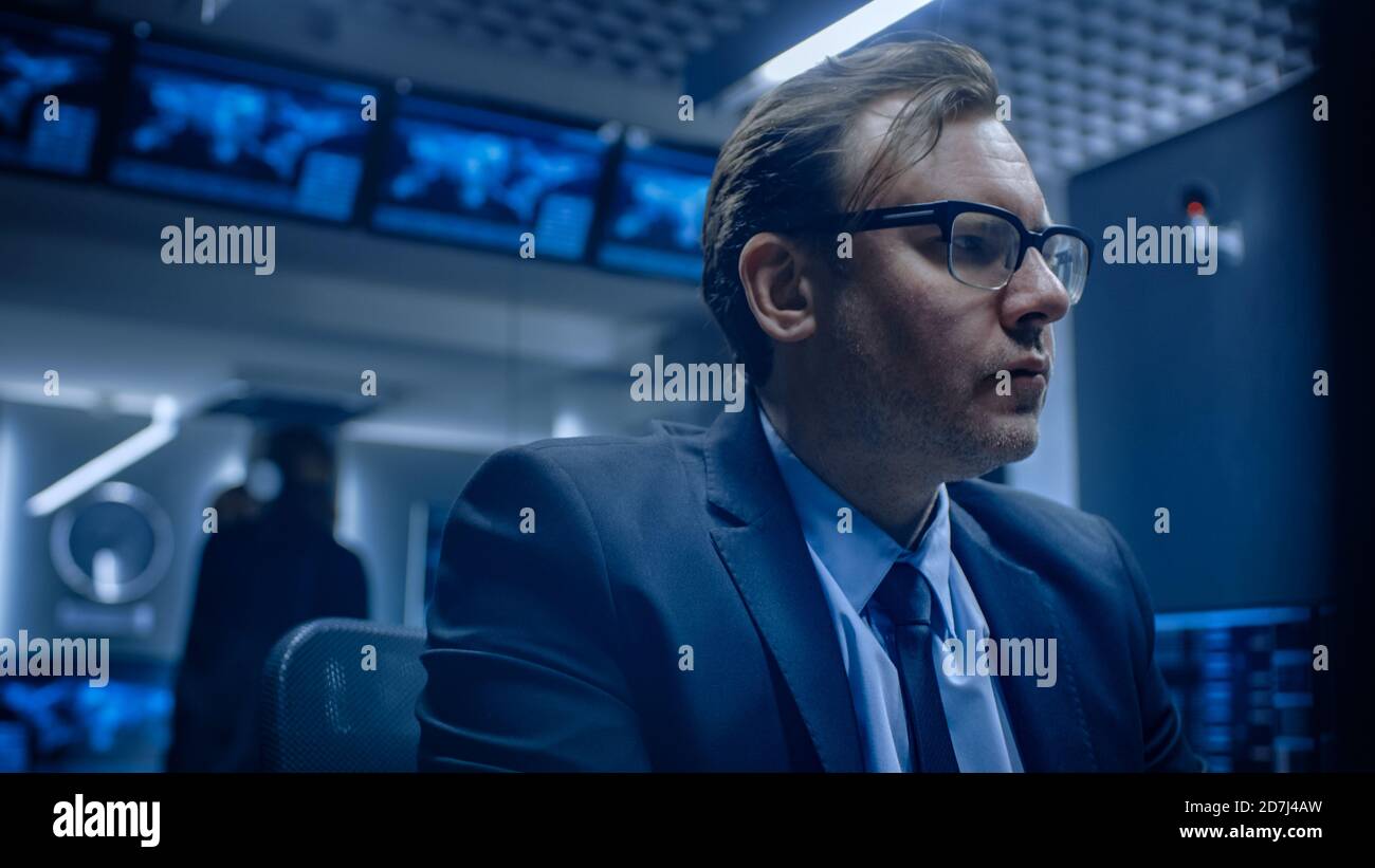 Niedriger Winkel des betroffenen Spezialisten, der am Computer im Überwachungskontrollraum arbeitet, mit Teams, die Probleme im Hintergrund lösen. Stockfoto