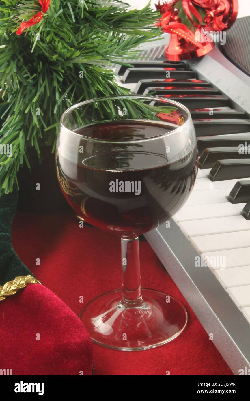 Glas Rotwein mit Klaviertasten und Weihnachtsschmuck im Hintergrund, in vertikalem Format Stockfoto