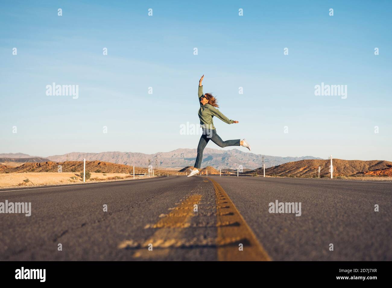 Sorglose Frau, die auf Wüstenstraße gegen Himmel springt, Nevada, USA Stockfoto