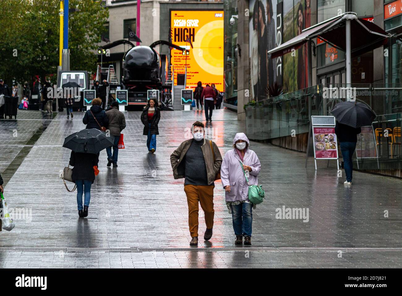 Ein Mann und eine Frau gehen in der New Street in Birmingham mit Gesichtsmasken entlang, da sich die Stadt bei Regenwetter in Covid Alert Tier 2, High Alert, befindet Stockfoto
