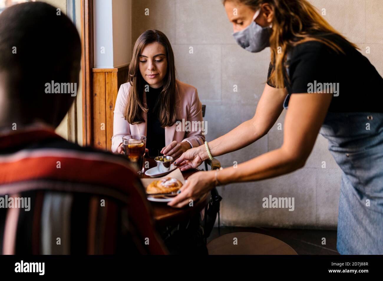 Kellnerin in schützende Gesichtsmaske serviert Essen zu jungen Paar Im Café während der COVID-19 Stockfoto