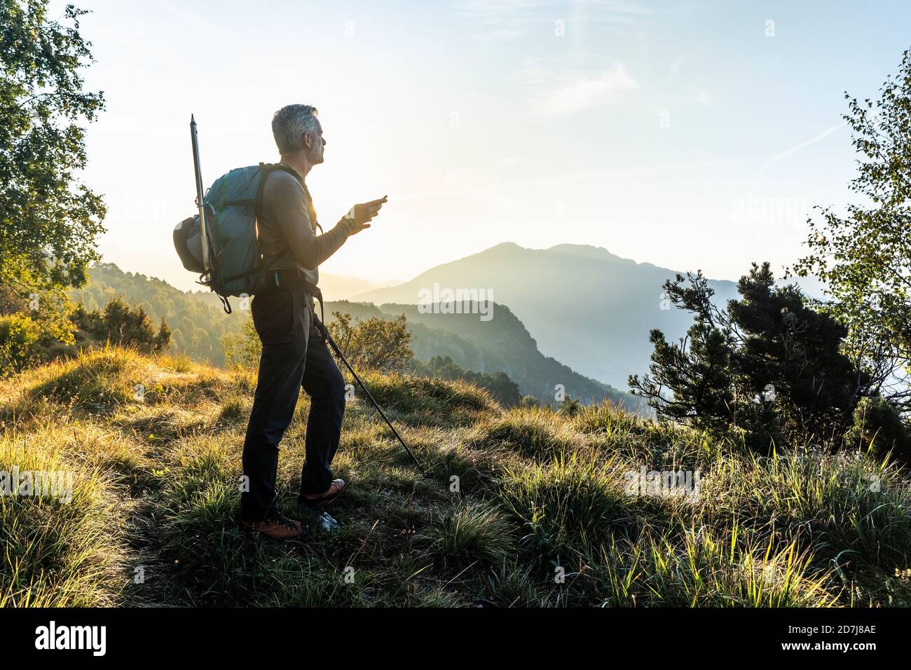 Mann mit Handy, während auf dem Berg gegen den Himmel bei Sonnenaufgang, Orobie, Lecco, Italien Stockfoto