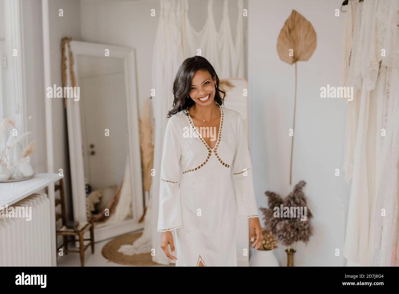 Lächelnde junge Braut steht im Geschäft für Hochzeitskleid Stockfoto