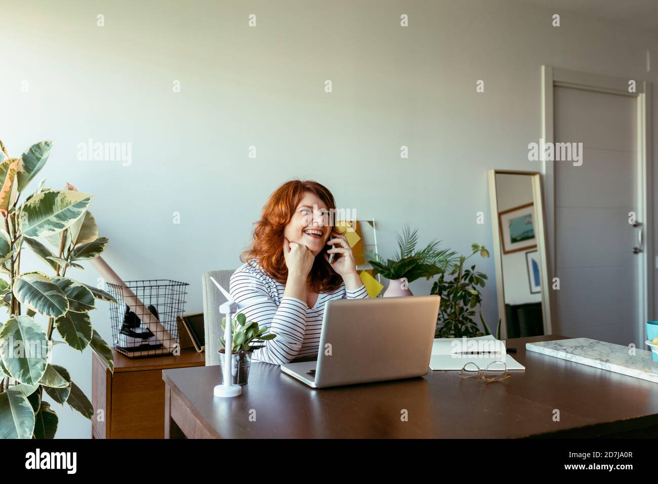 Frau lächelt, während sie zu Hause telefoniert Stockfoto