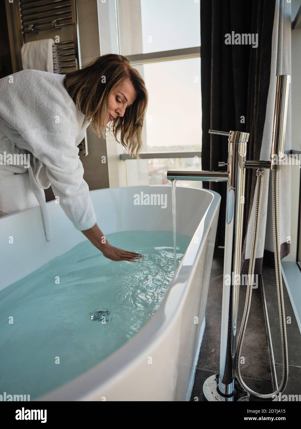 Ältere Frau, die sich bei der Untersuchung der Temperatur in der Badewanne beugte Luxushotel Stockfoto