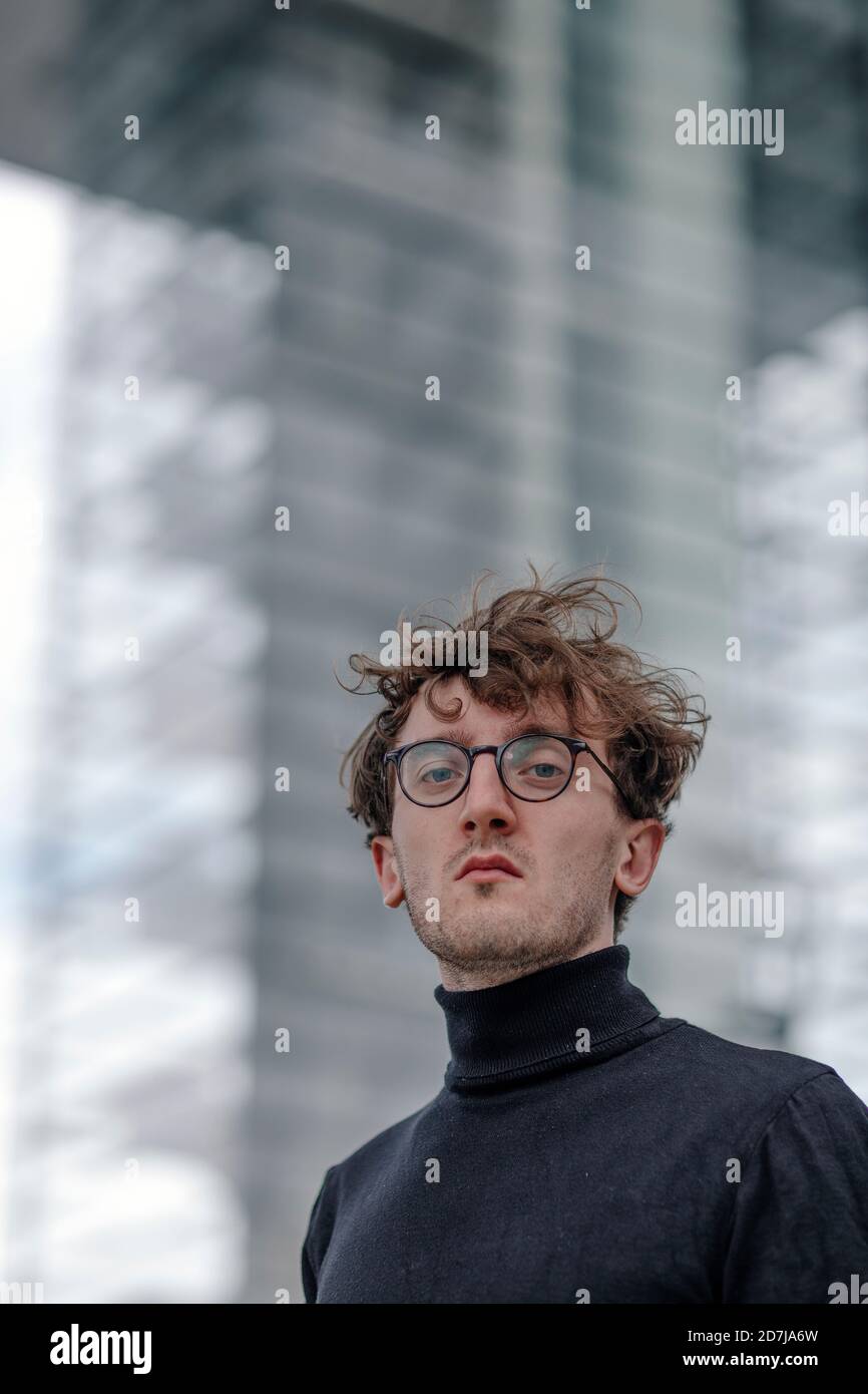 Nahaufnahme eines ernsthaften jungen Mannes, der eine Brille gegen das Gebäude trägt Stockfoto