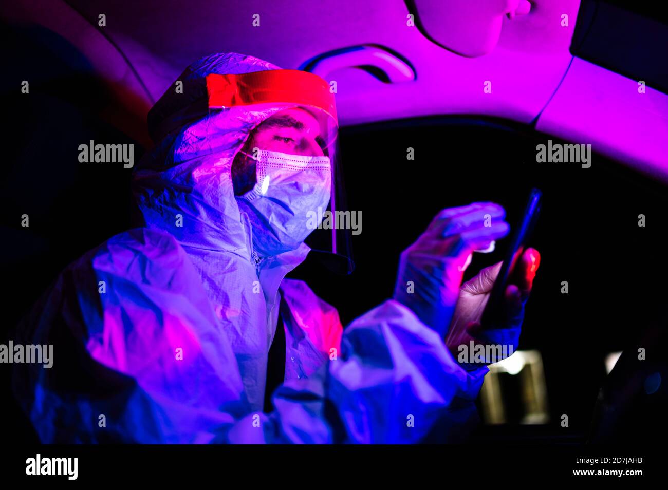 Mann trägt Schutzanzug mit Smartphone im Krankenwagen bei Nacht Stockfoto