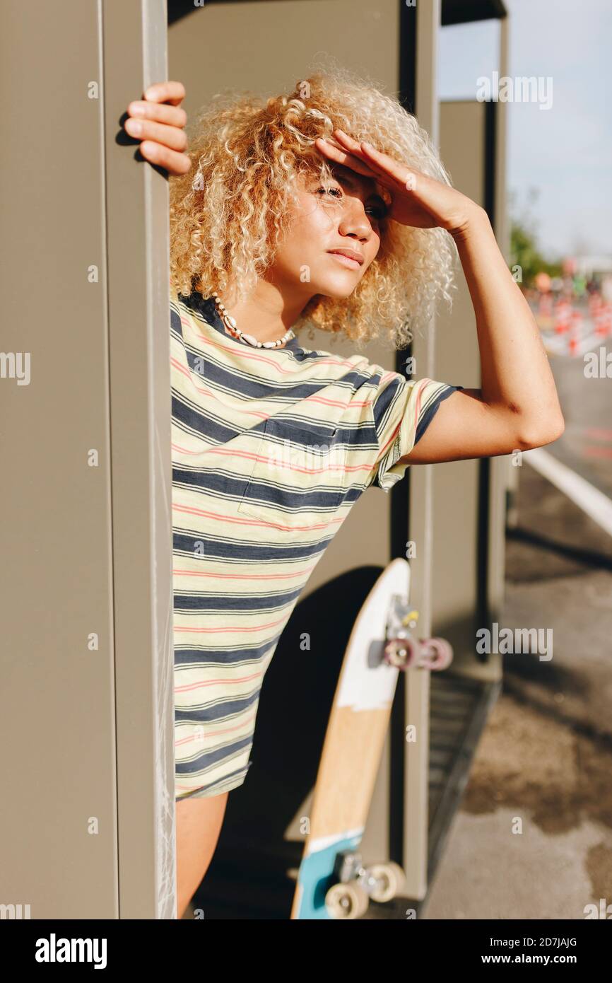 Blonde Afro Frau, die Augen abschirmt, während sie von metallischen weg schaut Wand an sonnigen Tag Stockfoto