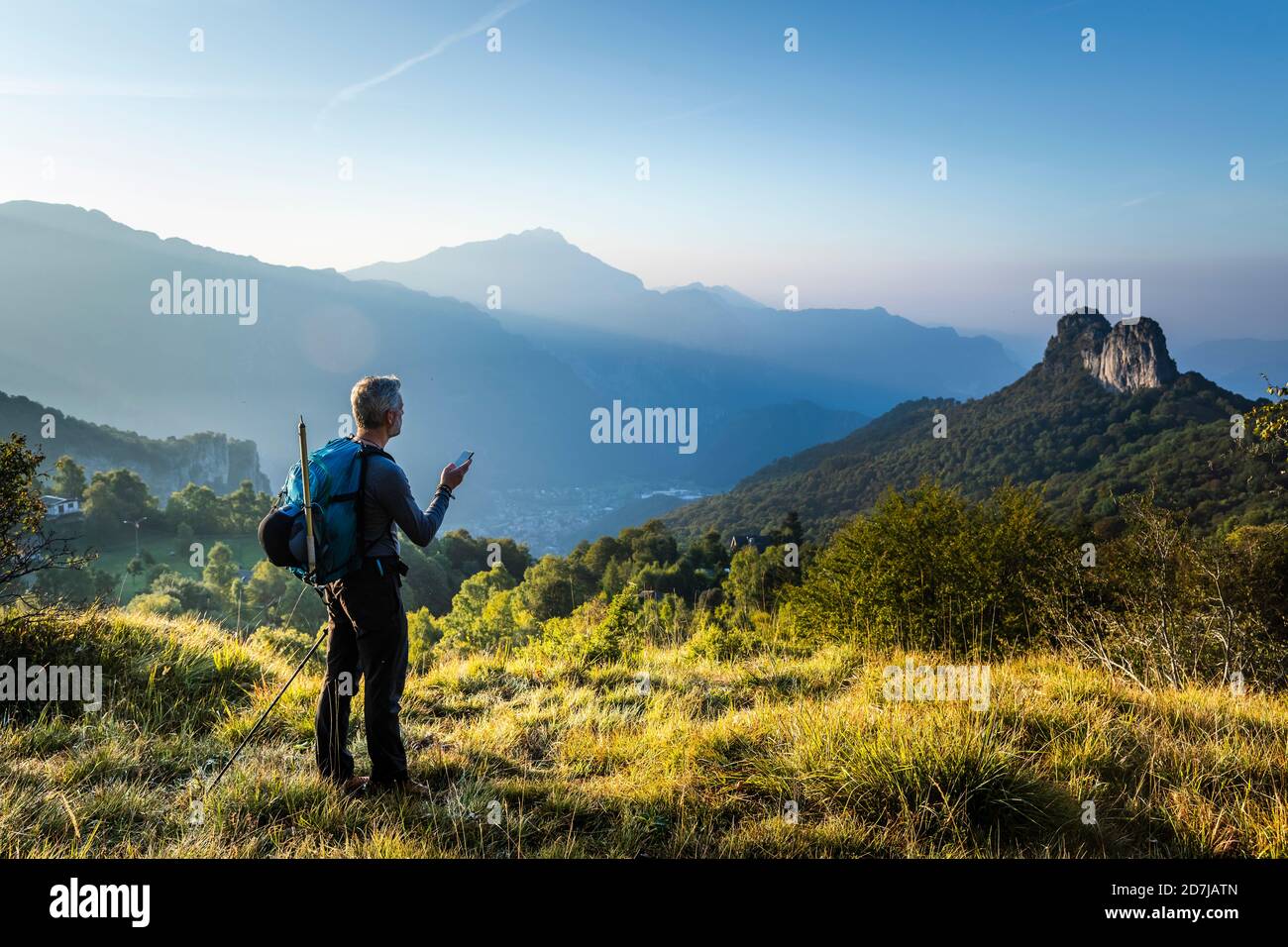 Mann mit Rucksack mit Handy, der während des Sonnenaufgangs auf dem Berg steht, Orobie, Lecco, Italien Stockfoto