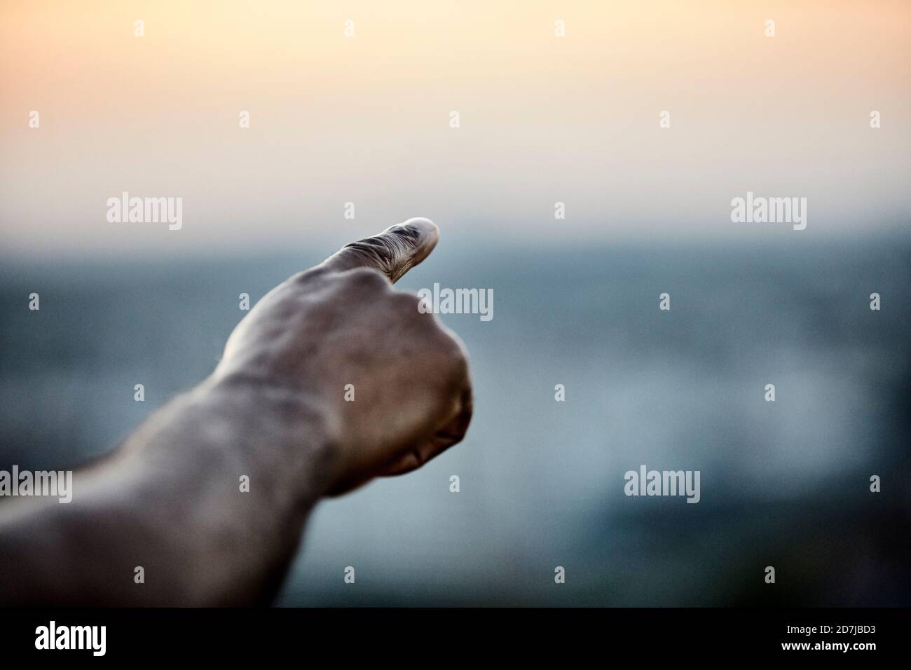 Von der Terrasse aus auf den Himmel zeigende, beschnittene Hand des Mannes Bei Sonnenuntergang Stockfoto