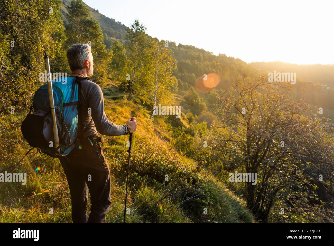 Reifer Mann mit Rucksack, der bei Sonnenaufgang auf dem Berg am Wald steht, Orobie, Lecco, Italien Stockfoto