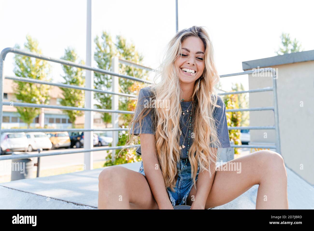 Fröhliche Frau mit langen blonden Haaren sitzt im Skateboard Park Stockfoto