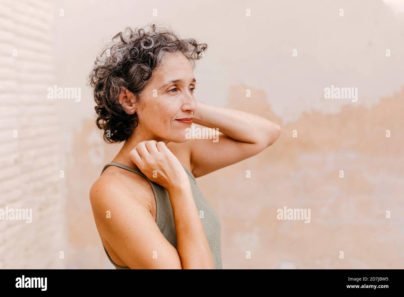 Reife Frau mit Hand im Haar, die gegen die Wand steht Stockfoto