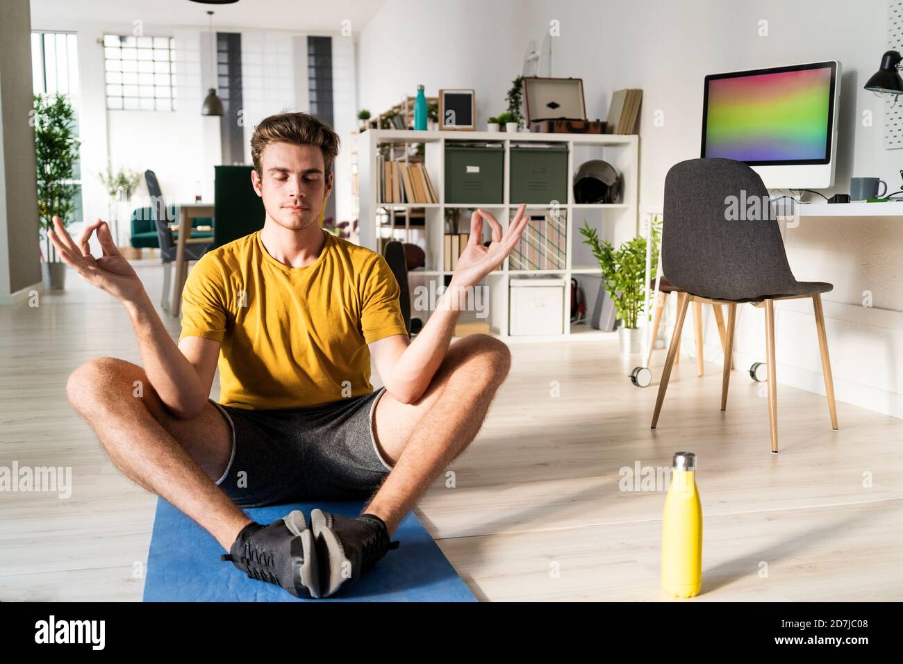 Junger Mann, der Yoga praktiziert, während er zu Hause auf der Matte sitzt Stockfoto