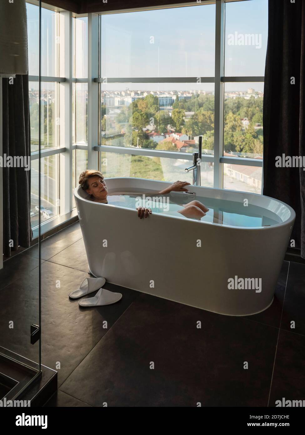 Frau, die im Luxushotel in der Badewanne vor dem Fenster baden Zimmer Stockfoto