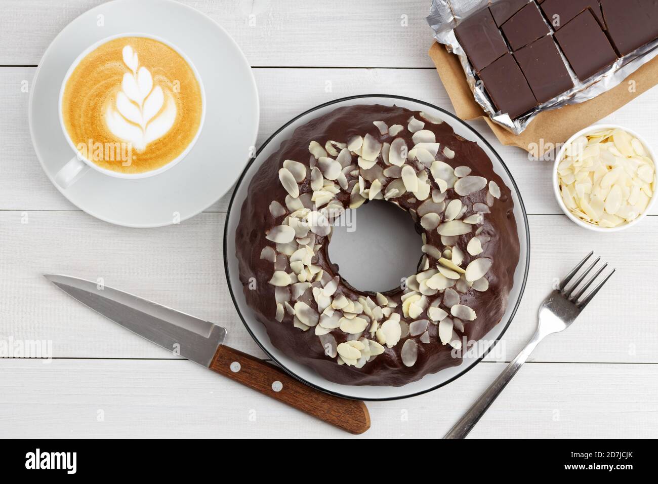 Hausgemachter Schokoladenkäsekuchen mit Mandelscheiben und Tasse Kaffee Cappuccino auf weißem Holztisch. Draufsicht. Stockfoto
