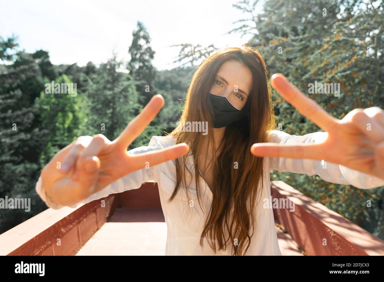 Junge Frau trägt schützende Gesichtsmaske tun Hand Geste, während Im Balkon stehend Stockfoto