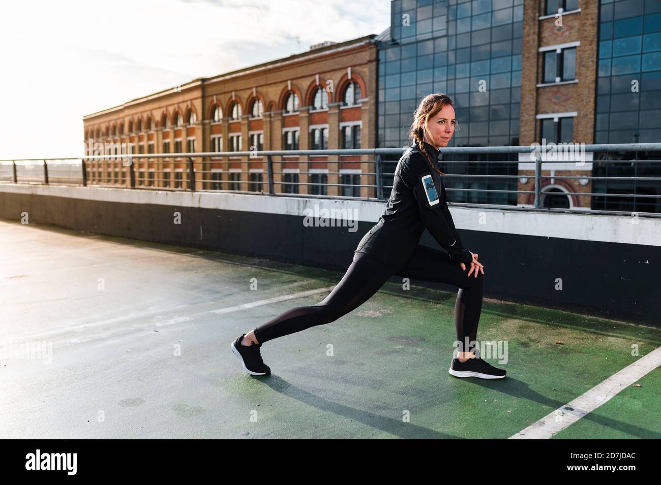 Weibliche Sportlerin, die die Beine auf dem Dach gegen Gebäude in der Stadt streckt Stockfoto