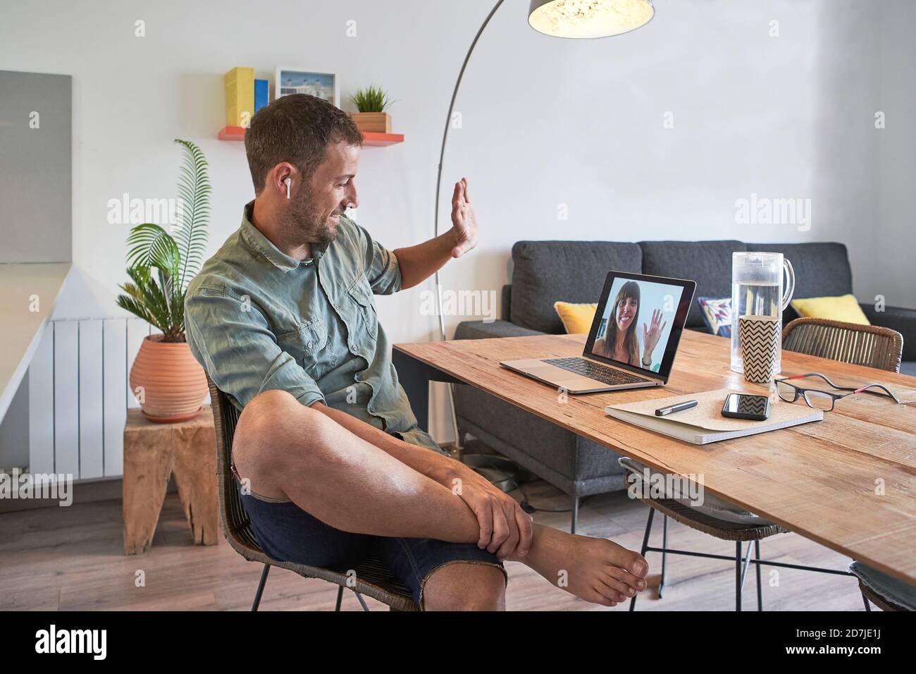 Lächelnder, gutaussehender Geschäftsmann winkt einer Kollegin per Videoanruf zu Auf dem Laptop, während Sie von zu Hause aus arbeiten Stockfoto