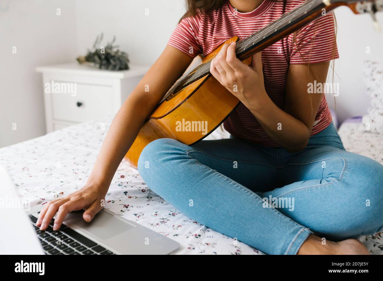 Frau, die online Gitarre spielen lernt, während sie im Schlafzimmer sitzt Zu Hause Stockfoto