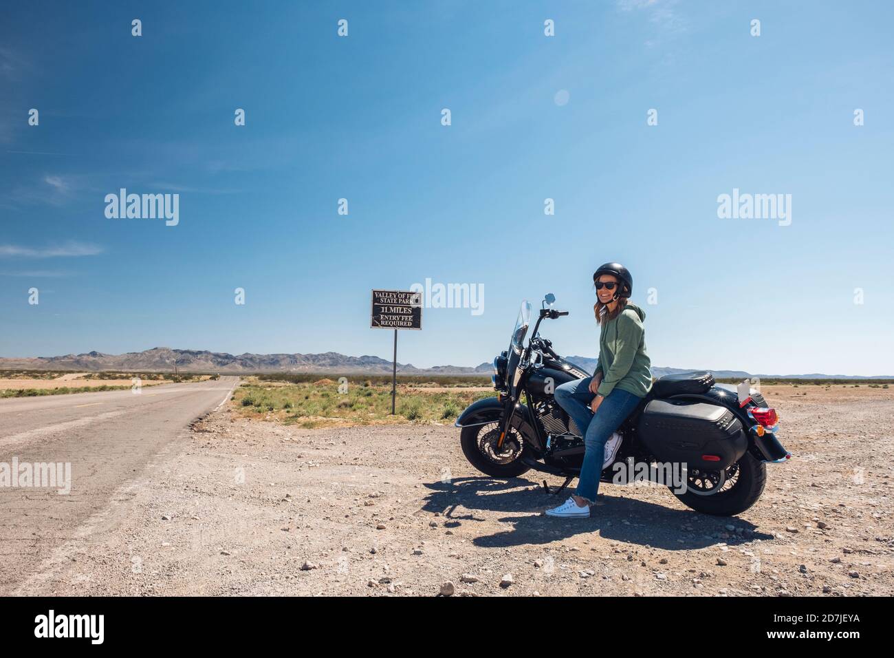 Frau sitzt auf dem Motorrad durch Wüstenstraße gegen Himmel während der Reise, Nevada, USA Stockfoto