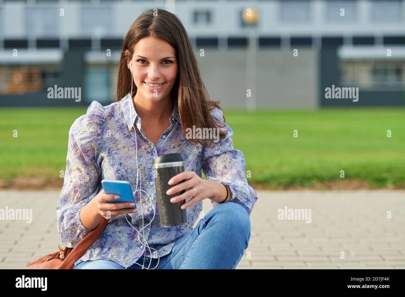 Lächelnde Frau mit Handy, während sie auf dem Fußweg sitzt Stadt Stockfoto
