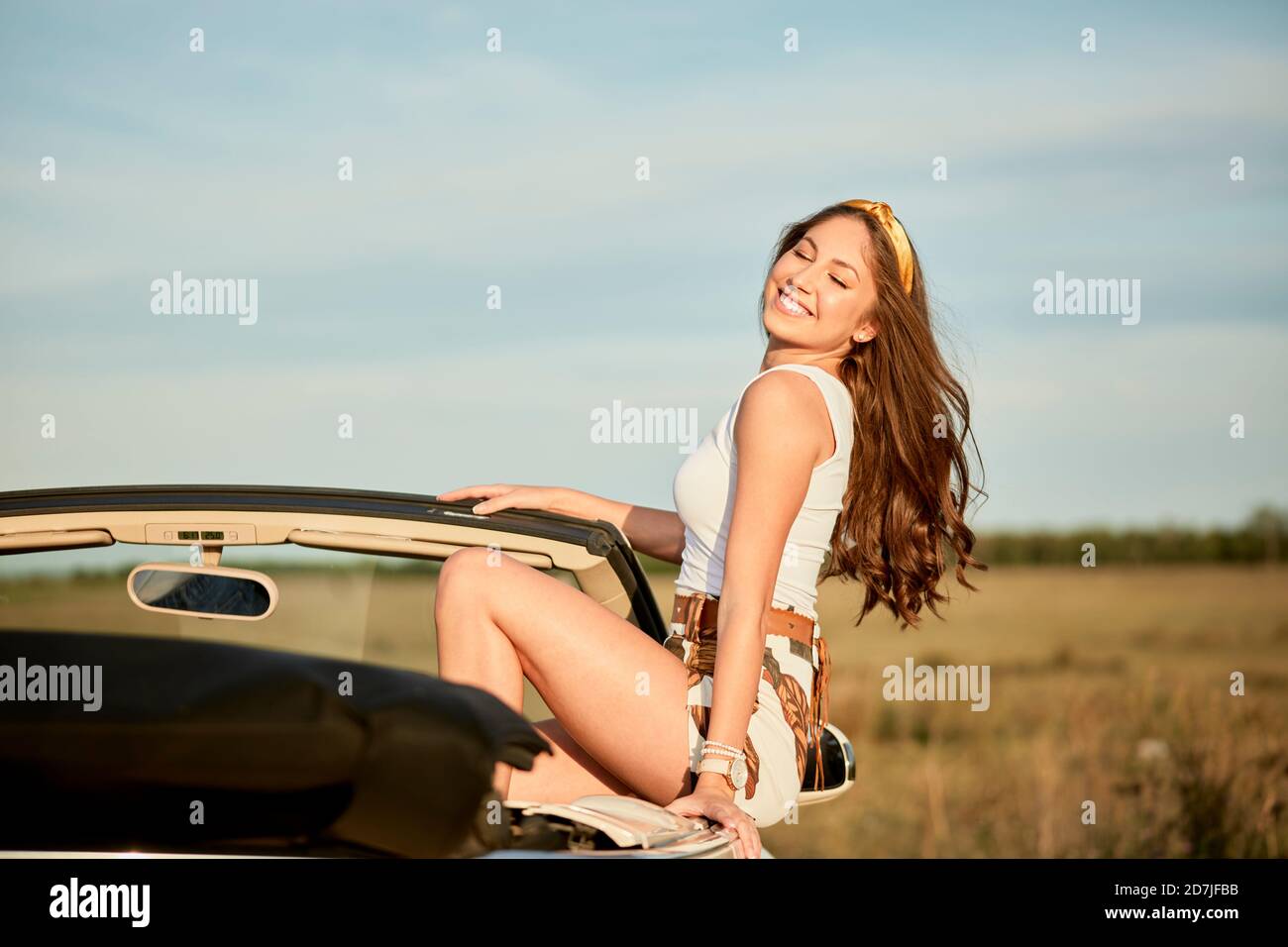 Lächelnde Frau mit langen Haaren sitzt auf Luxus-Auto Stockfoto