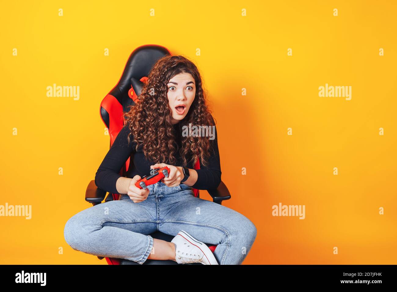 Frau, die hinter einem Spielstuhl in ihren Händen sitzt und rot hält Gamepad auf gelbem Hintergrund Stockfoto