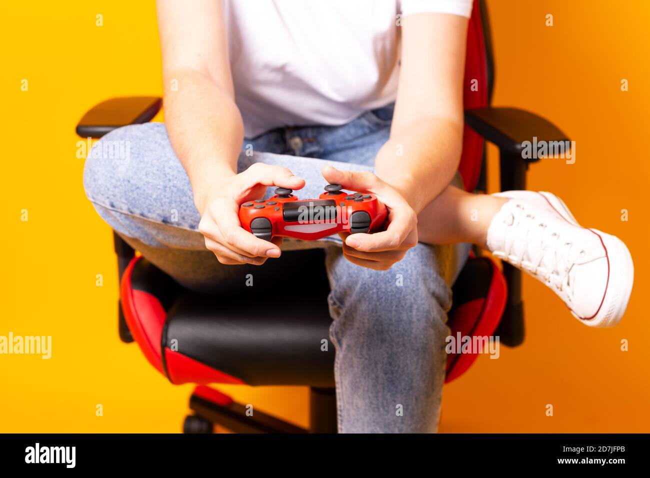 Frau, die hinter einem Spielstuhl in ihren Händen sitzt und rot hält Gamepad auf gelbem Hintergrund Stockfoto