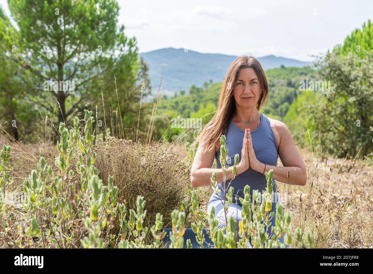 Schöne Frau, die Yoga praktiziert, während sie auf dem landwirtschaftlichen Feld hockend Stockfoto