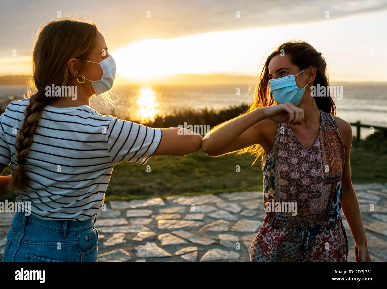Frauen in schützenden Gesichtsmasken Ellbogen stoßen gegen den Himmel während COVID-19-Ausbruch Stockfoto