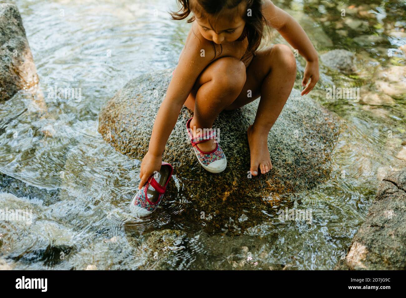Nettes Mädchen spielen in fließendem Wasser, während auf Felsen sitzen Im Sommer Stockfoto
