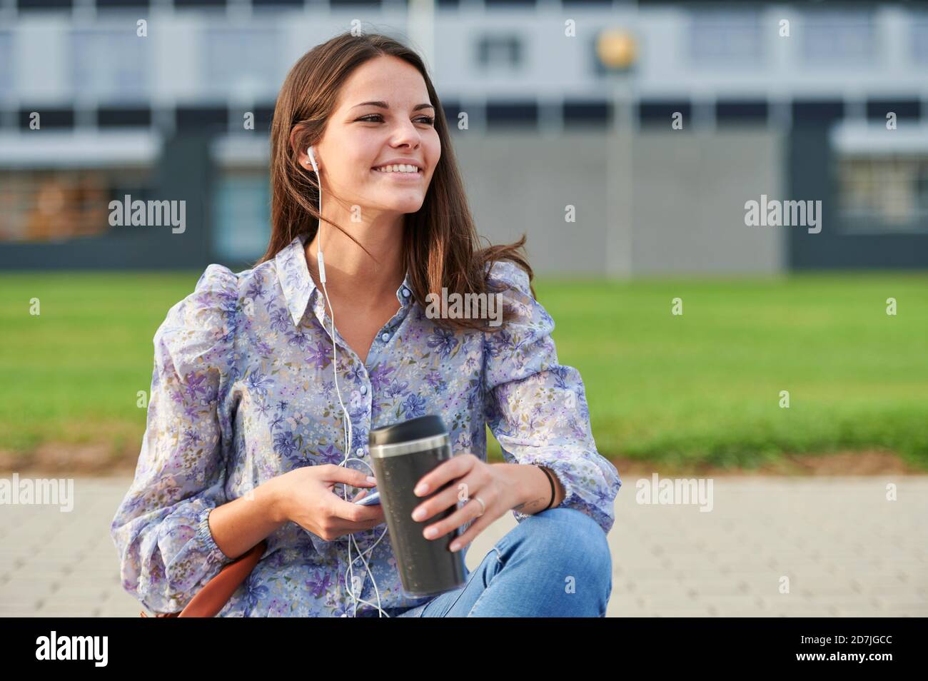 Junge Frau mit Handy, während sie auf dem Fußweg sitzt Stadt Stockfoto