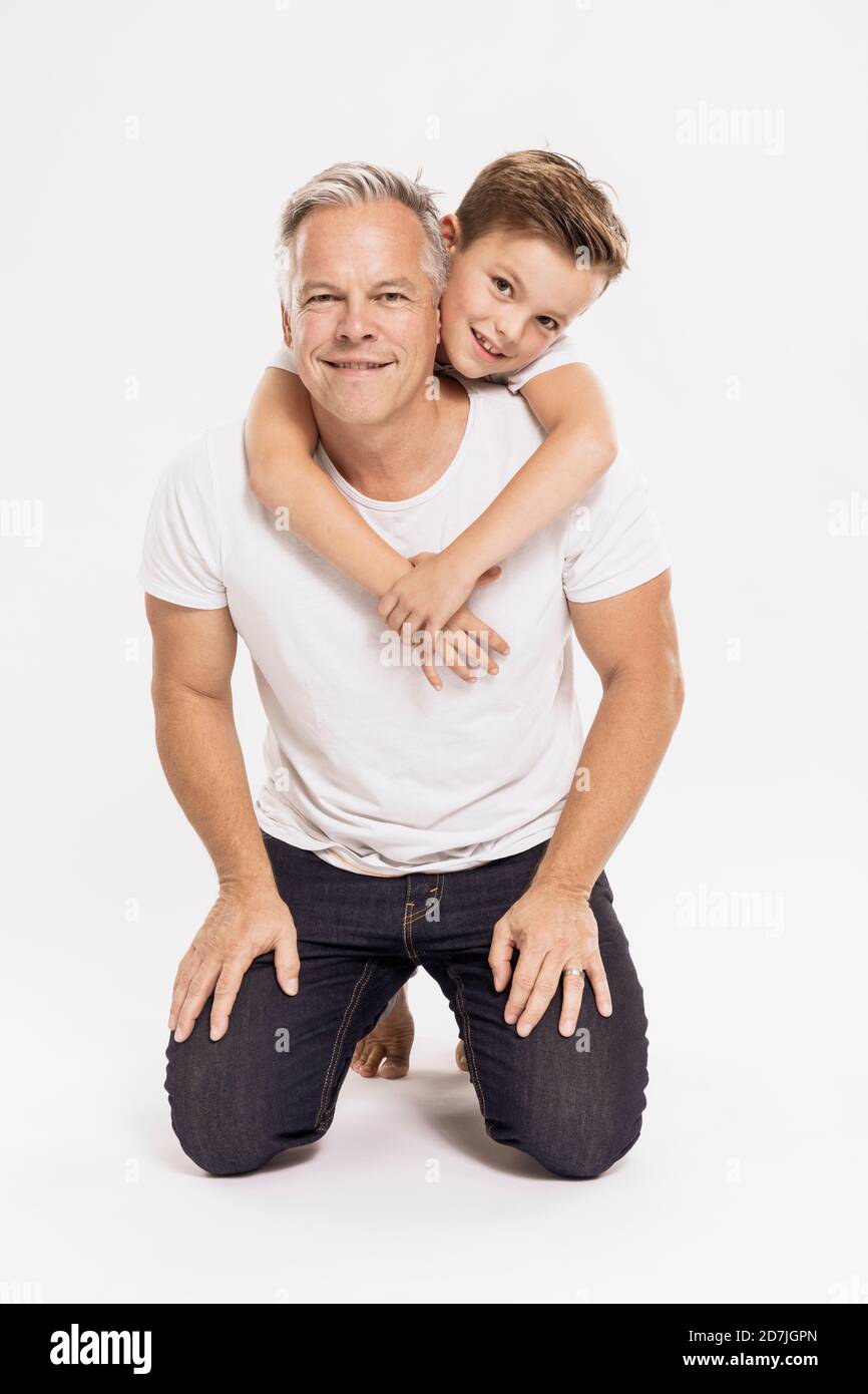 Netter Junge umarmt Vater kniend vor weißem Hintergrund Stockfoto
