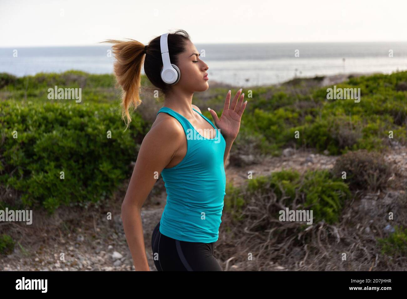 Junge Lateinerin, die Musik hört, während sie in der Nähe des Meeres joggt Stockfoto