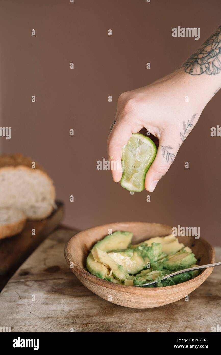 Frau Hand quetscht Limette in Avocado-Salat auf Schneiden gehalten Brett in der Küche Stockfoto