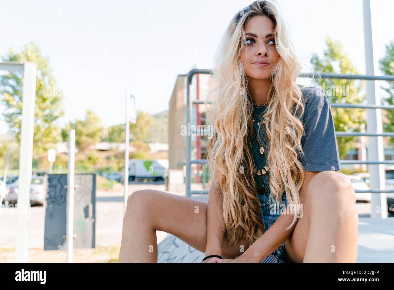 Nachdenkliche Frau mit langen blonden Haaren schaut weg, während sie sitzt Im Skateboard Park Stockfoto