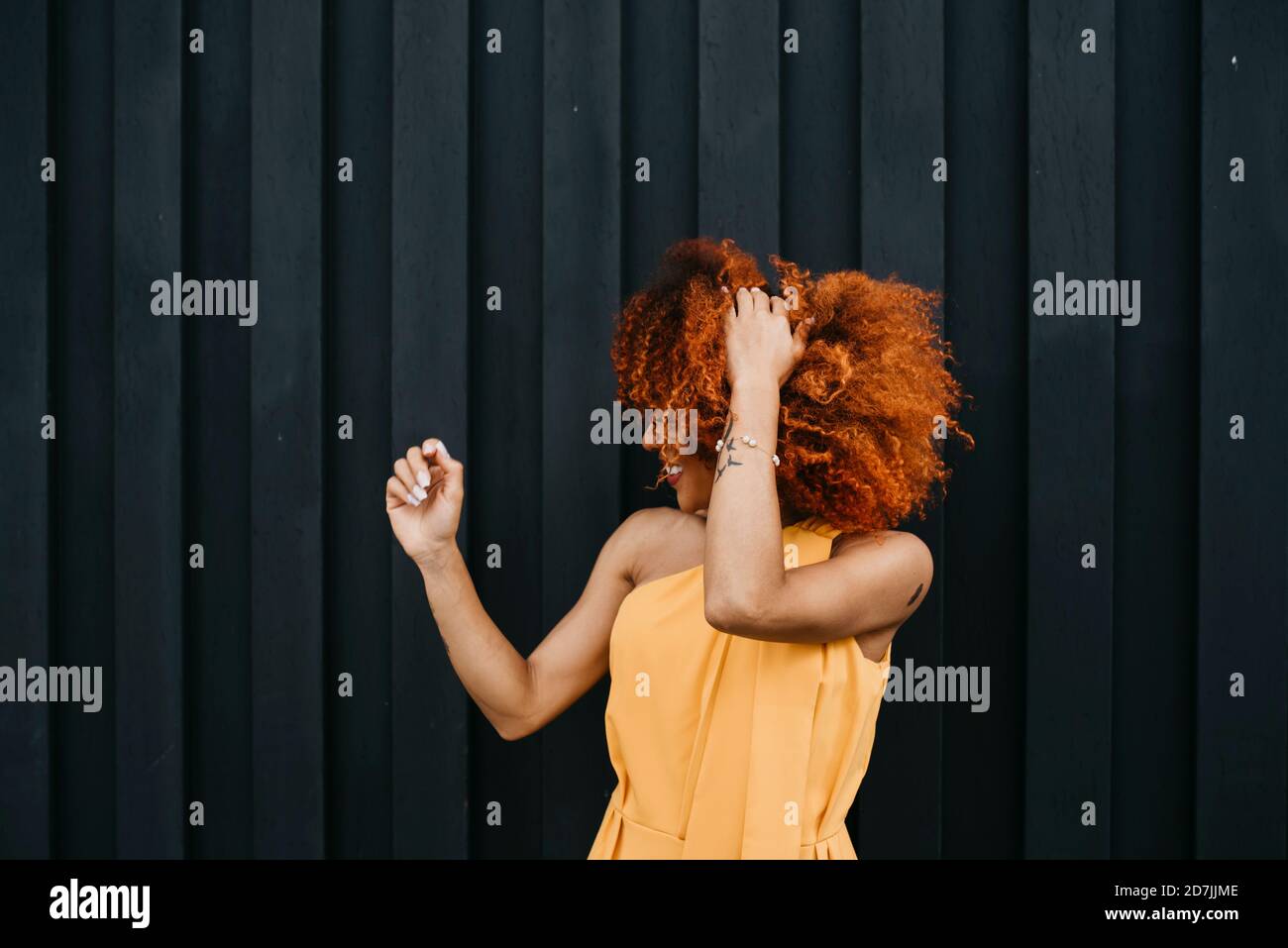 Fröhliche junge Frau schüttelt die Haare, während sie an der Wand steht Stockfoto